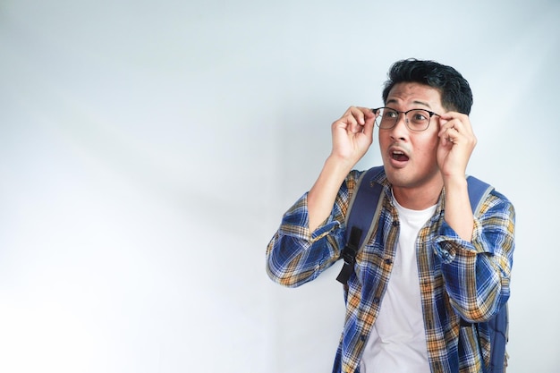 Excitado joven asiático estudiante en ropa casual mochila gafas mirando a un lado en el área de trabajo