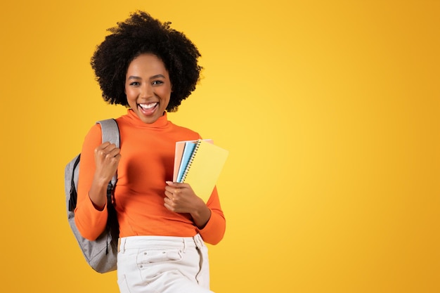 Excitado joven estudiante con un afro sonriendo ampliamente sosteniendo cuadernos