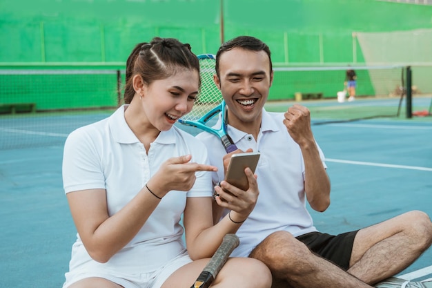 Excitados duplas tenistas usando telefones celulares juntos enquanto estão sentados