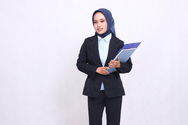 Exclusiva mujer de oficina asiática con hijab de pie alegremente en su lado derecho llevando un bolígrafo cl