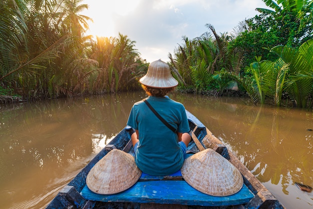 Excursión en barco en la región del Delta del río Mekong, Ben Tre, Vietnam del Sur. Turista con sombrero vietnamita en crucero en el canal de agua a través de la plantación de cocoteros.