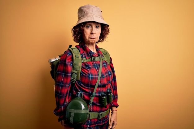 Excursionista de cabello rizado de mediana edad mujer caminando con mochila y cantimplora de agua usando binoculares deprimida y preocupada por la angustia llorando enojada y asustada Expresión triste