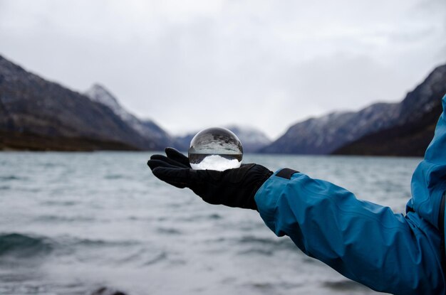 Un excursionista con una esfera de vidrio que refleja las montañas que rodean el lago gjende