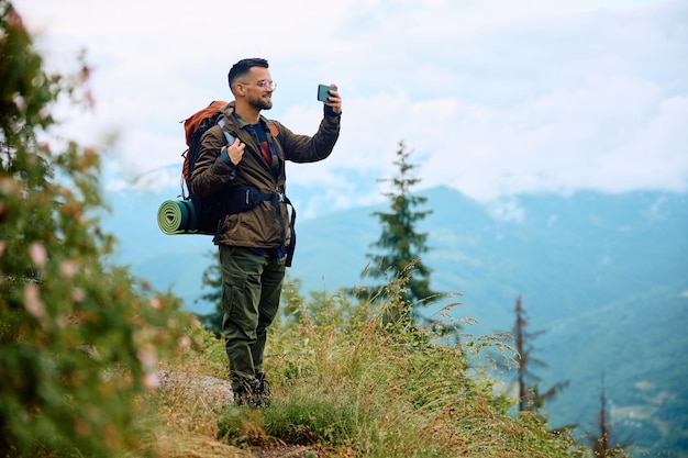 Excursionista feliz usando teléfono móvil mientras toma fotos de la naturaleza