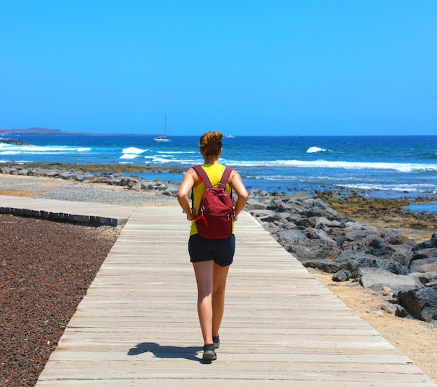 Foto excursionista femenina caminando sobre la pasarela con el espectacular paisaje de la playa de playa de las américas, tenerife, españa