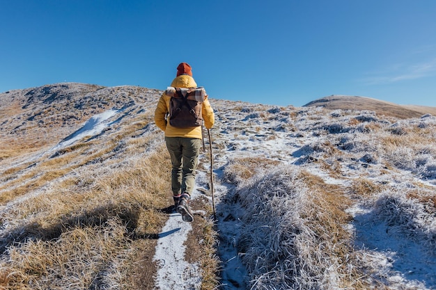 Excursionista femenina escalando una colina nevada de la cordillera contra las montañas y el cielo azul claro