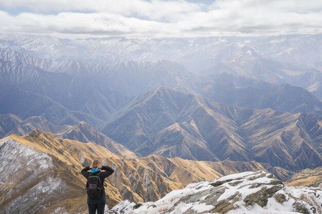 Una excursionista femenina de pie en la cima de la montaña disfrutando de las vistas de las cadenas montañosas delante de ella