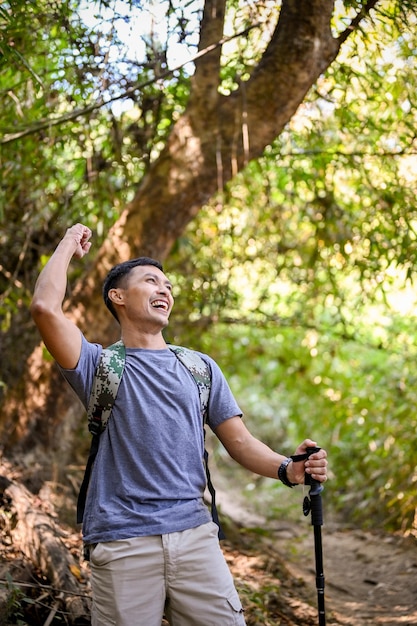 Excursionista masculino asiático emocionado y activo levantando la mano celebrando el éxito llegó al destino