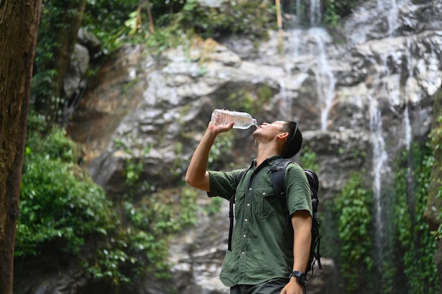 Foto un excursionista masculino con una mochila bebiendo agua de una botella cerca de una cascada de montaña