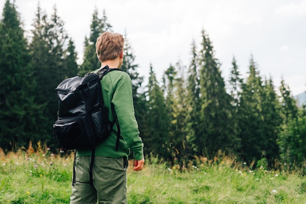 Excursionista masculino en ropa casual y mochila sube montañas vista trasera Un hombre en una caminata camina en un prado en las montañas