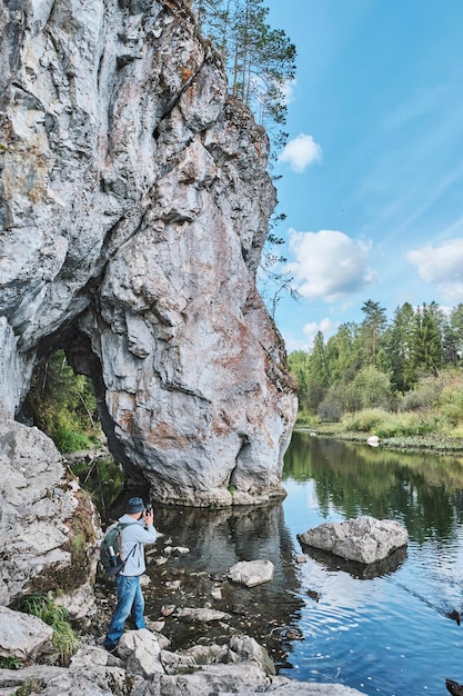 Excursionista masculino senior tomando fotos en el teléfono móvil en la orilla del río cerca de la roca Paisaje natural de verano