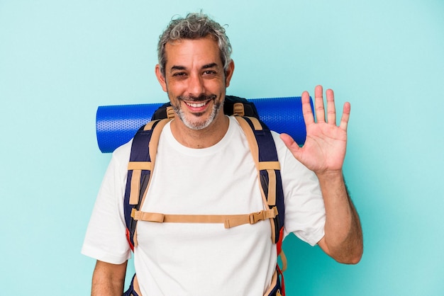 Excursionista de mediana edad hombre caucásico aislado de fondo azul sonriendo alegre mostrando el número cinco con los dedos.