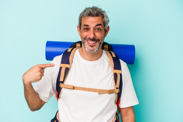 Excursionista de mediana edad hombre caucásico aislado sobre fondo azul persona apuntando con la mano a un espacio de copia de camisa, orgulloso y seguro