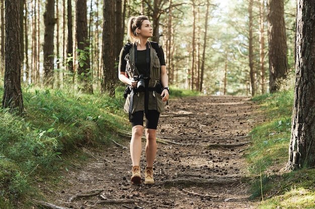 Excursionista de mujer caminando con una mochila y una moderna cámara sin espejo en bosque verde