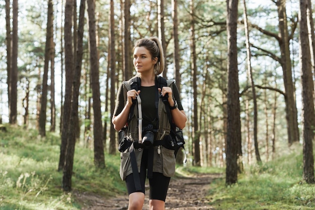 Excursionista mujer caminando con una mochila y una moderna cámara sin espejo en bosque verde