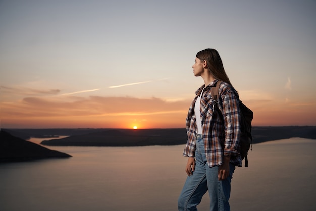 Excursionista mujer con mochila admirando la hermosa puesta de sol