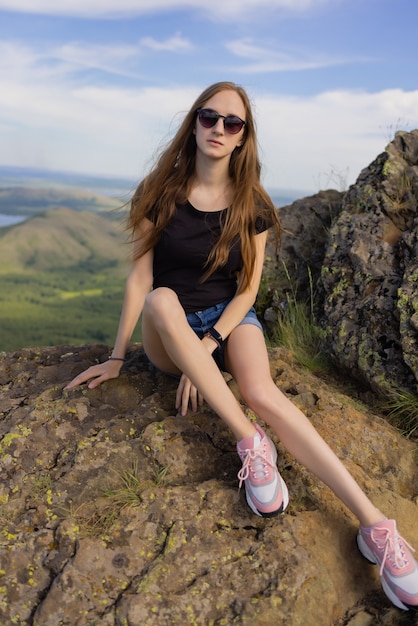 Excursionista mujer con mochila sentado en la cima de la montaña disfrutando de la vista durante el día.