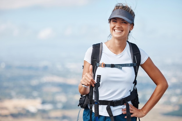 Excursionista mujer senderismo y pulgares arriba al aire libre con una sonrisa en la aventura retrato viajes y éxito trekking montaña Fitness libertad y feliz de ganar mochilero y turista en la naturaleza