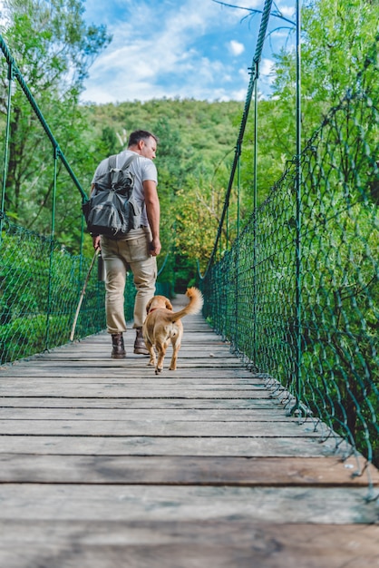 Excursionista con perro caminando sobre puente colgante de madera