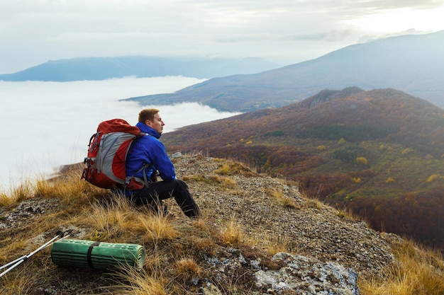 Excursionista turístico con mochila relajándose en la cima de la montaña mirando el paisaje puesta de sol sobre las nubes