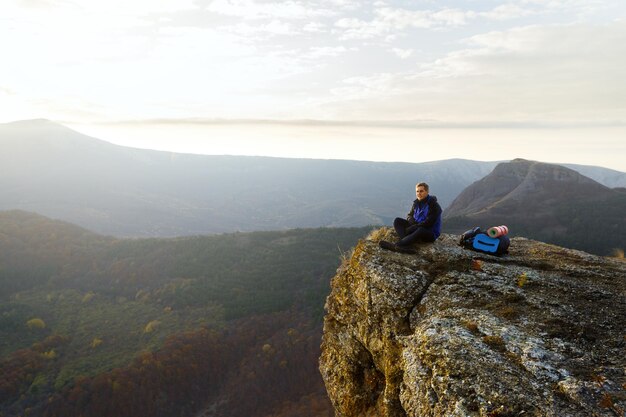 Excursionista turístico con mochila relajándose en la cima de la montaña mirando el paisaje puesta de sol sobre las nubes