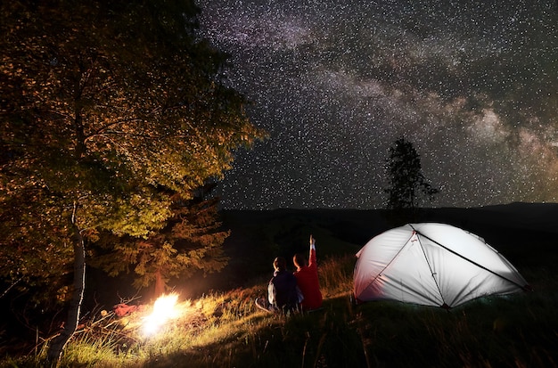 Excursionistas cerca de fogatas y carpas en el campamento nocturno.