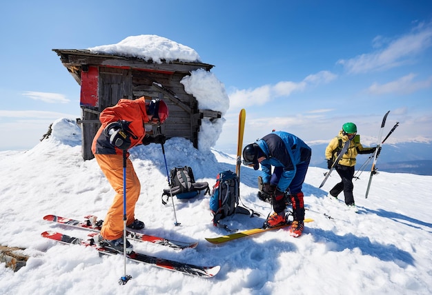 Excursionistas en equipo de esquí en la cima de una colina nevada ajustando los esquís en el paisaje montañoso de fondo