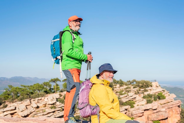 Excursionistas mayores felices con mochilas disfrutando de las vistas del valle desde la cima de una montaña