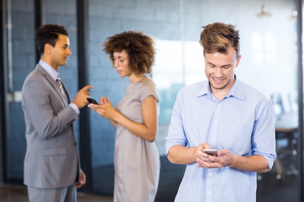 Executivo confiante usando telefone celular com seus colegas de trabalho