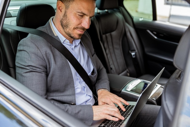 Foto executivo de negócios trabalhando em laptop no carro durante o deslocamento matinal