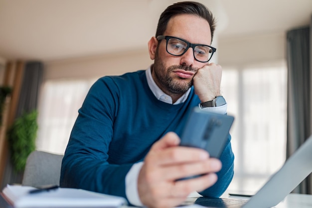 Executivo entediado usando telefone inteligente enquanto trabalhava na mesa do escritório