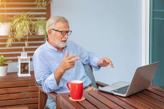 Executivo sênior com cabelos brancos usando teleconferência de computador portátil em casa com café