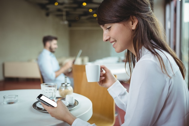 Foto executivo usando telefone celular enquanto toma café no refeitório