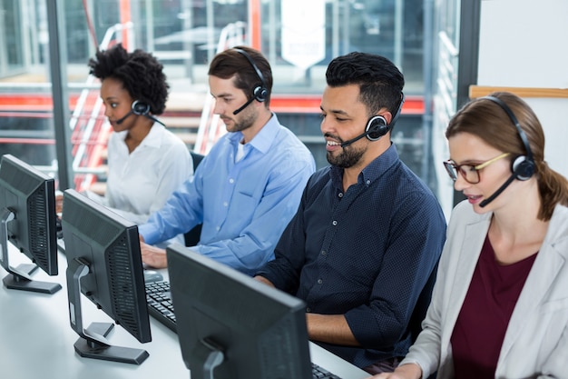 Executivos de negócios com fones de ouvido usando computadores na mesa no escritório