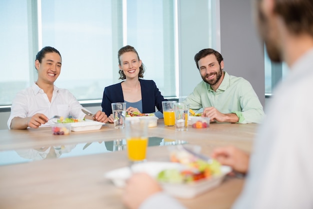 Executivos sorridentes fazendo uma refeição no escritório