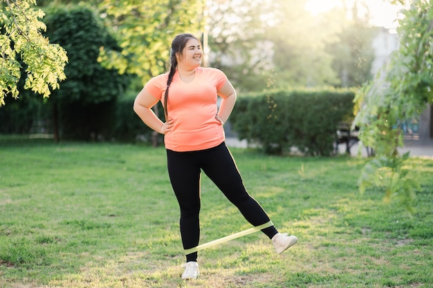 Exercício de banda Controle de peso Estilo de vida ativo Corpo positivo Mulher obesa com excesso de peso motivada feliz em treinamento de fitness esportivo na paisagem verde ensolarada do parque primavera