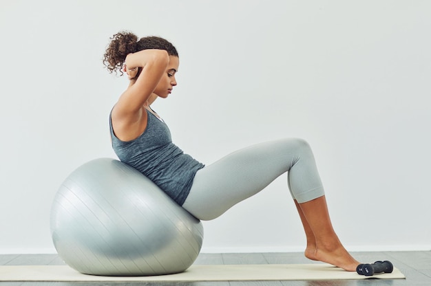 Exercício de bola e sentar-se com a mulher no estúdio em fundo branco para força central bem-estar ou treino Treinamento de aptidão e perfil de pessoa com equipamento para equilíbrio saúde ou estabilidade