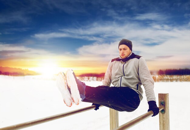 Foto exercício de fitness, desporto e conceito de pessoas jovem fazendo exercício abdominal em barras paralelas no inverno