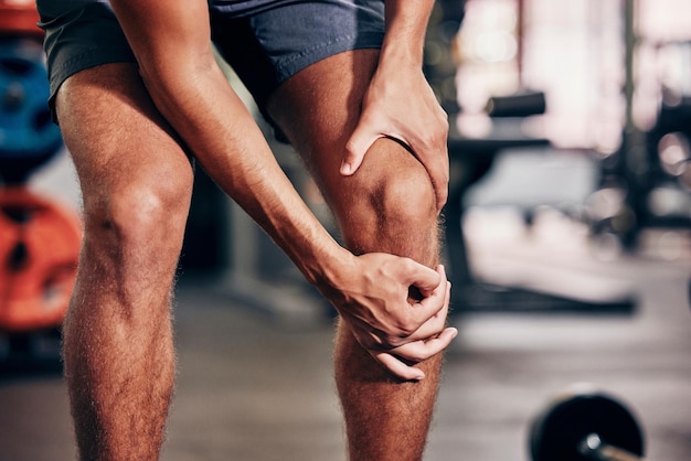 Foto exercício de fitness e homem com dor no joelho no ginásio, segurando a perna após acidente de lesão e dor muscular esportes de saúde e atleta do sexo masculino com dor nas articulações após o exercício de treino e treinamento