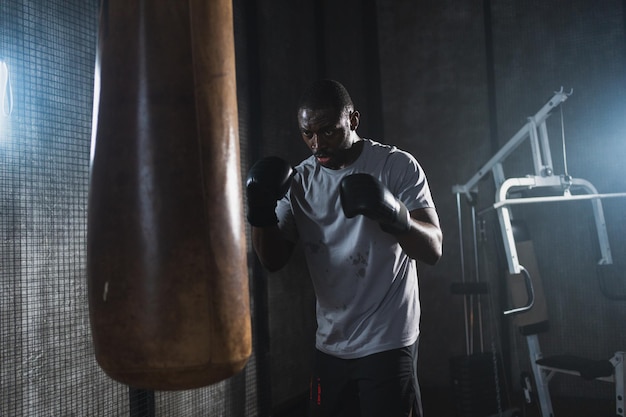 Exercício de fitness no ginásio homem africano forte treinamento de combate socos com saco de boxe homem boxeador saudável