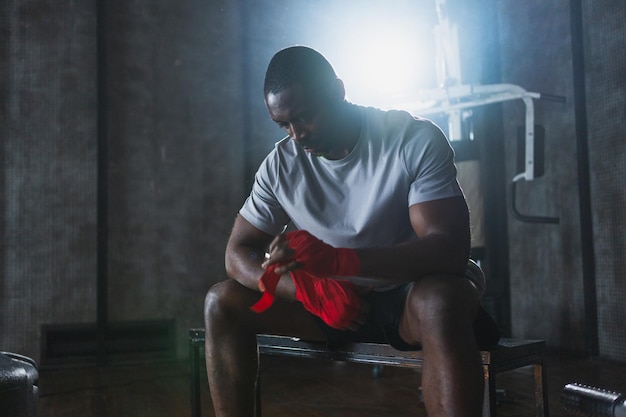 Exercício de fitness no ginásio homem afro-americano lutador preparando-se para a luta envolvendo as mãos com vermelho