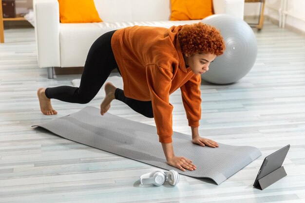 Exercício de fitness treino jovem saudável em forma garota africana fazendo exercícios esportivos em tapete de ioga no chão