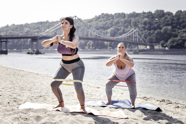 Exercício útil. Mulheres bonitas e bonitas a fazer abdominais com elástico enquanto fazem exercício ao ar livre