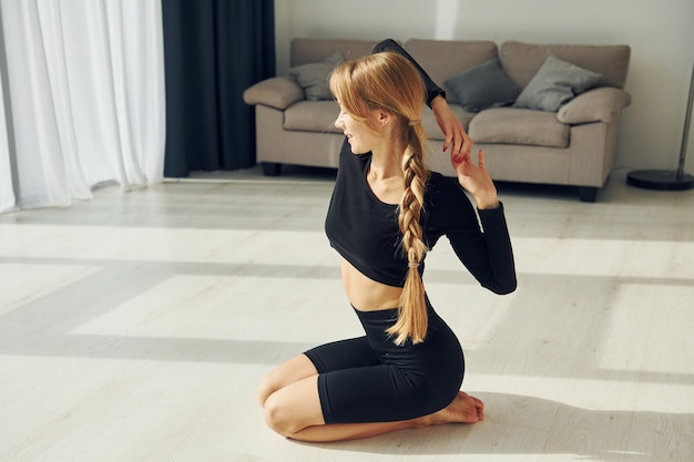 Exercícios de alongamento Mulher em roupas esportivas fazendo ioga dentro de casa