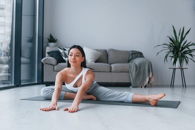 Exercícios de ioga Jovem com forma de corpo esbelto em roupas esportivas tem dia de fitness dentro de casa