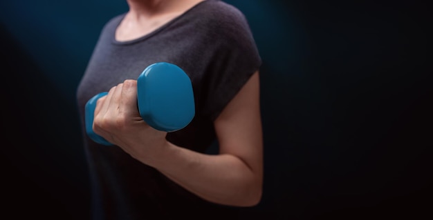 Exercitando treino com halteres esporte e recreação conceito closeup de mulher com halteres azul no quarto escuro em casa ou ginásio