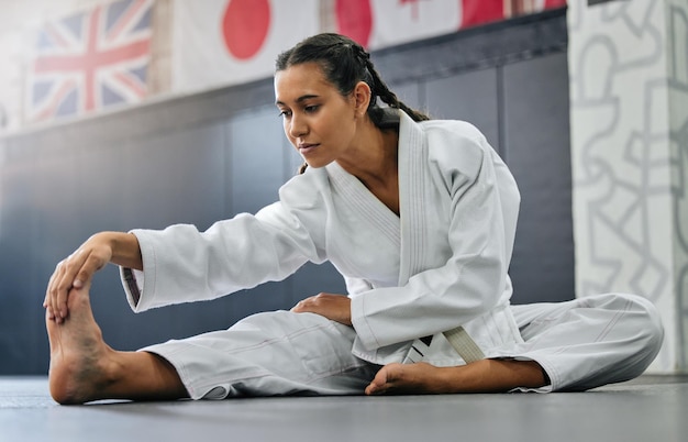 Exercite luta e treino de alongamento de um estudante de escola de karatê com foco antes do início do treinamento Mulher esportiva ou treinador se alongando para um exercício em um ginásio de performance de estúdio de dojo ou clube de artes marciais