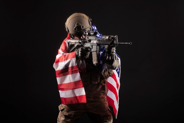 Foto exército da américa um soldado em equipamento militar com uma arma segura a bandeira dos eua em um fundo preto