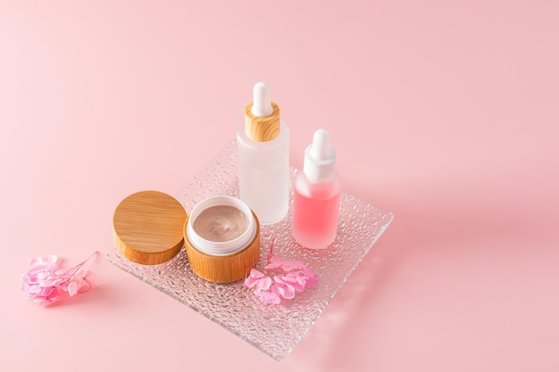 Exfoliante corporal en un frasco de bambú abierto y dos cosméticos en botellas blancas mate con un cuentagotas para el cuidado natural de la piel de la cara y el cuerpo Fondo rosa