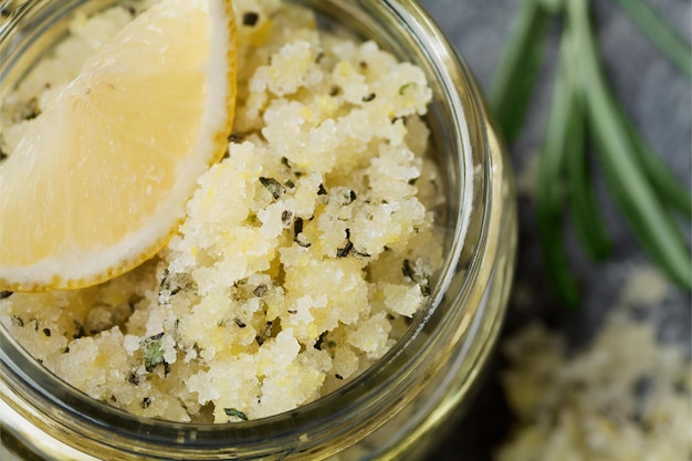 Exfoliante corporal de sal marina con limón, romero y aceite de oliva en frasco de vidrio sobre mesa de piedra cosm casero